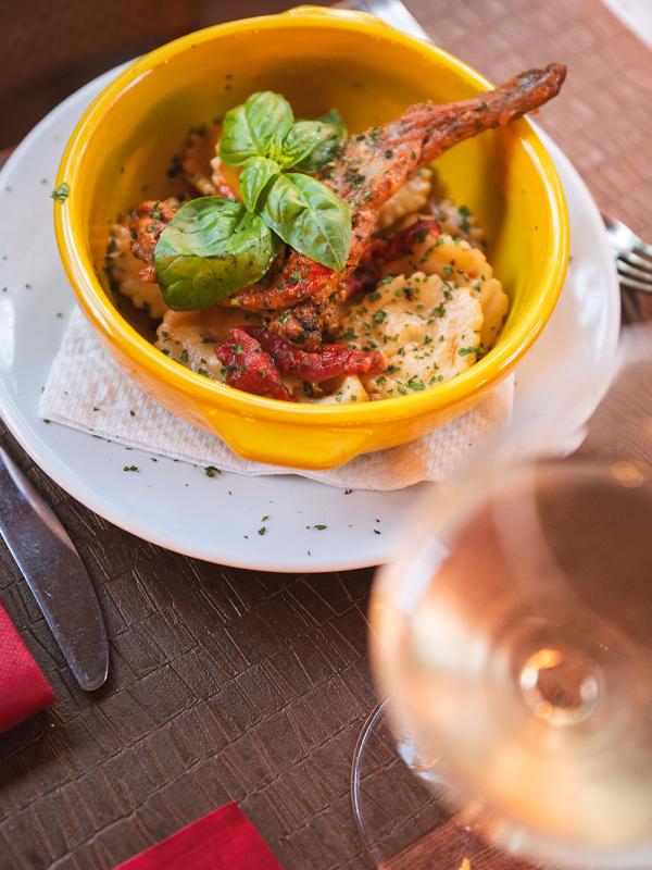 Pasta ripiena con carne e basilico in ciotola gialla, bicchiere di vino.